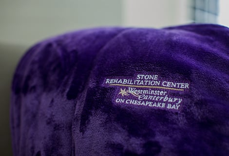A plush purple cushion with Stone Rehabilitation Center and Westminster Canterbury on Chesapeake Bay embroidered in white and lavender text.