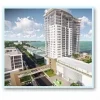 Aerial view of a tall white building, likely a modern hotel or apartment complex, near a coastal area. The structure features balconies and large windows. The sky is partly cloudy, and the nearby street is visible with some greenery.