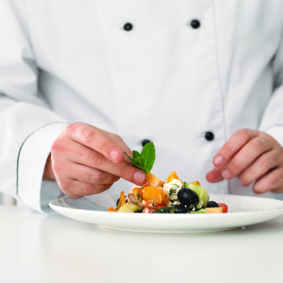 A chef proudly presents a colorful salad on a plate, showcasing fresh ingredients and culinary skill.